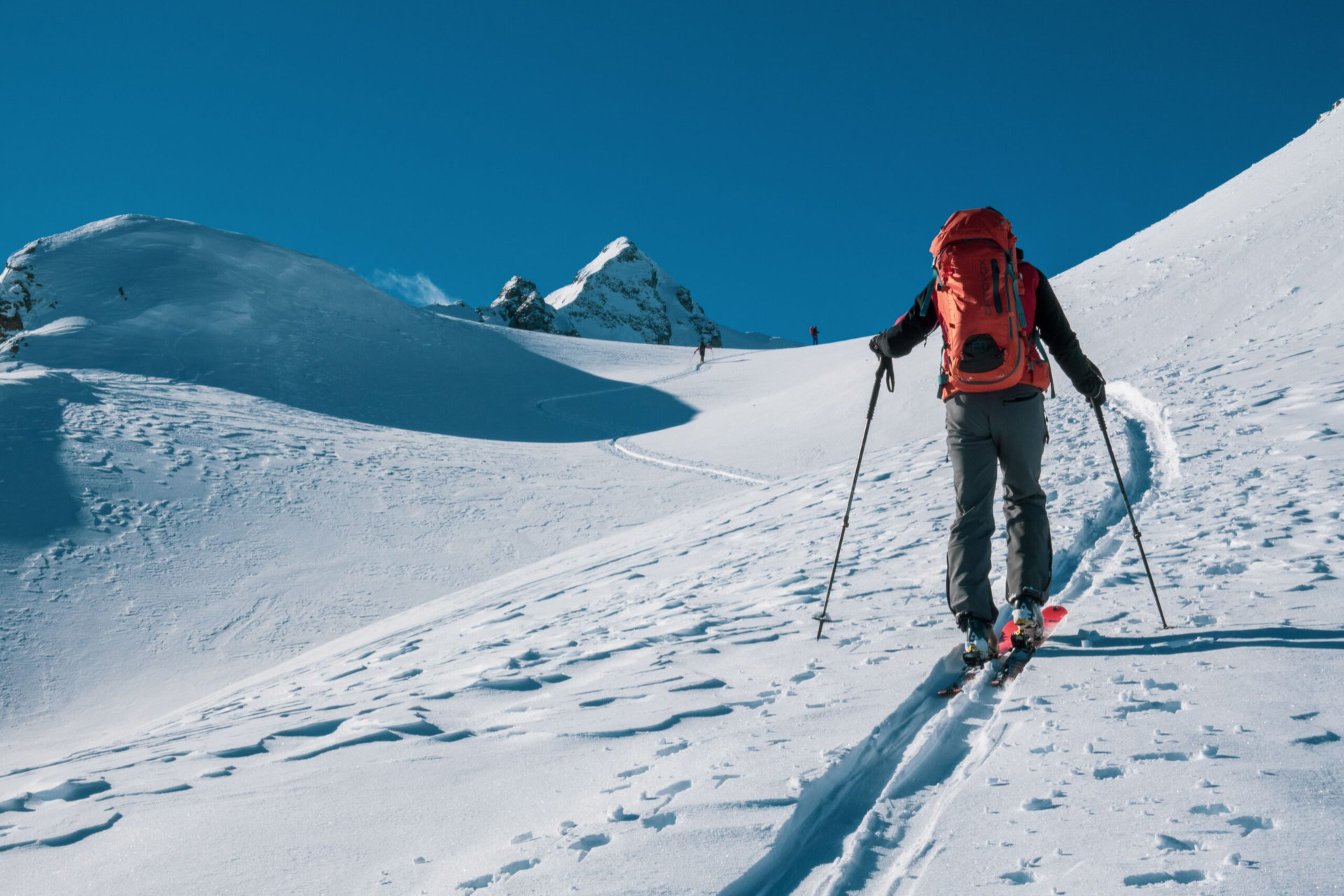 Skieur de randonnée en montée sur une pente enneigée, sous un ciel bleu