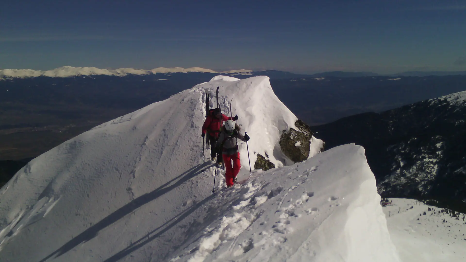 randonneurs ski sur une arête enneigée se suivent en file indienne sur un sommet.